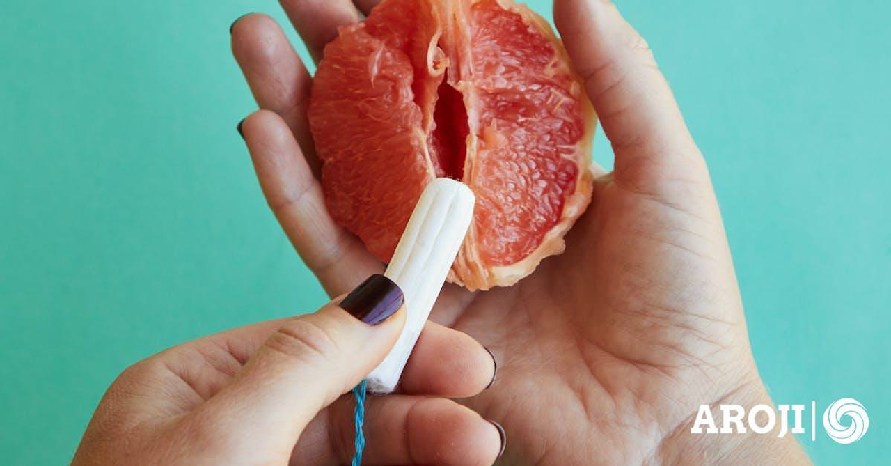 From above of crop anonymous female demonstrating on sliced ripe grapefruit correct use of tampon against blue background